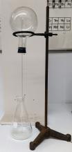 Empty set up of a round flask secured upside down by a ring stand, sealed with a two-hole stopper. Below the round flask is a large Erlenmeyer flask. A long glass tube runs from the Erlenmeyer into the round flask through one of the two rubber holes.