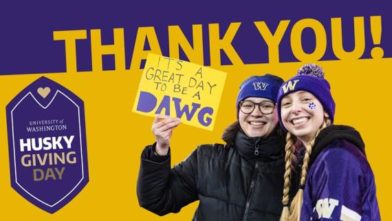 Two students wearing Husky gear smile for the camera holding a sign that reads "It's a great day to be a dawg."