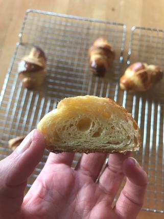 Crosscut of a croissant baked by Lizzy Canarie with three whole croissants on a cooling rack in the background.