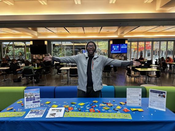 Arnette stands behind a table scattered flyers and colorful give-aways with his arms outstretched.