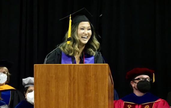 Lucinda Liu wearing a graduation cap and gown standing behind a lectern