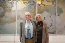 Prof. Campbell with his wife Professor Emeritus of Music Pat Campbell pose together in front of a piece of art.