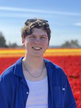 EJ Brannan wear sunglasses on top of his head and is pictured in front of a field of red, orange, and yellow tulips