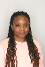 Elizabeth Momoh with long brown hair wearing a pastel colored sweater poses for the camera in front of a plain backdrop