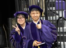 Two people wearing graduation regalia give a peace sign and a thumbs up