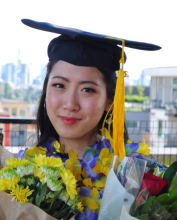 Emily Ding wearing a mortar board cap and gold tassel holds bouquets of flowers