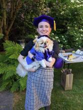 Emily in a tam and her pet dog dressed in doctoral robes.