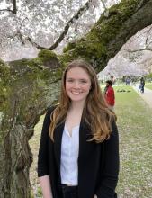 Katie MacNary wearing a dark blazer standing near a cherry blossom tree in full bloom
