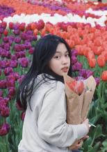 Ruibing Wu looks over her shoulder to face the camera as she stands among a field of tulips