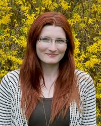 Kristen Darnell wears long red hair, glasses, and a striped sweater