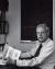 A black and white photo of Vandenbosch at his desk with a blackboard behind him.