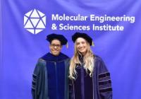 Al Nelson and Gokce Altin wear academic regalia and pose in front of a purple Molecular Engineering & Sciences Institute banner