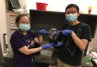 Two people wearing nitrile gloves and surgical masks touch a globe with their index fingers