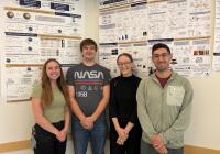 Three students and their mentor near large posters of their research