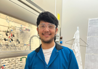 Adrian Guerrero poses in a chemistry lab wearing googles, a blue lab coat, and purple nitrile gloves.