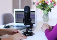 The hands of two people are visible on a table top where a microphone sits between them.