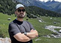 Johnathan Cox with arms folded, with snowy peaked mountains of Kyrgyzstan behind him.