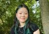 Mary Deng in a black tshirt near a tree smiles with a closed mouth