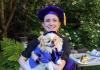 Emily in a tam and her pet dog dressed in doctoral robes.