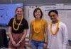 Three students stand side by side wearing yellow leis.