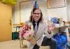 Tim holds up a balloon saying “congratulations”, a bouquet of flowers, and a mug with “Dr. Trinklein” written on it while wearing a party hat.