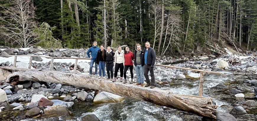 Seven people stand on a log bridge over the Nisqually River in Mt. Rainier National Park.