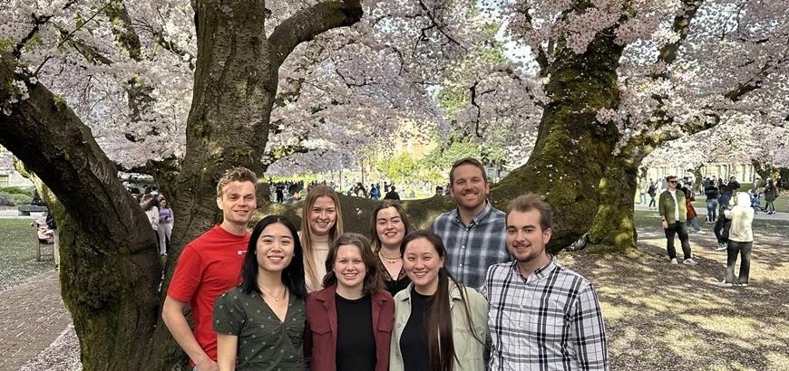 Eight people stand in front of a cherry blossom tree in full bloom.