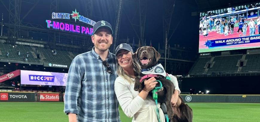 Nick poses with Shannon who holds the chocolate Labrador retriever on the field at T-Mobile Park.