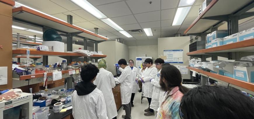 Eight people watch as a researcher uses a pipette.